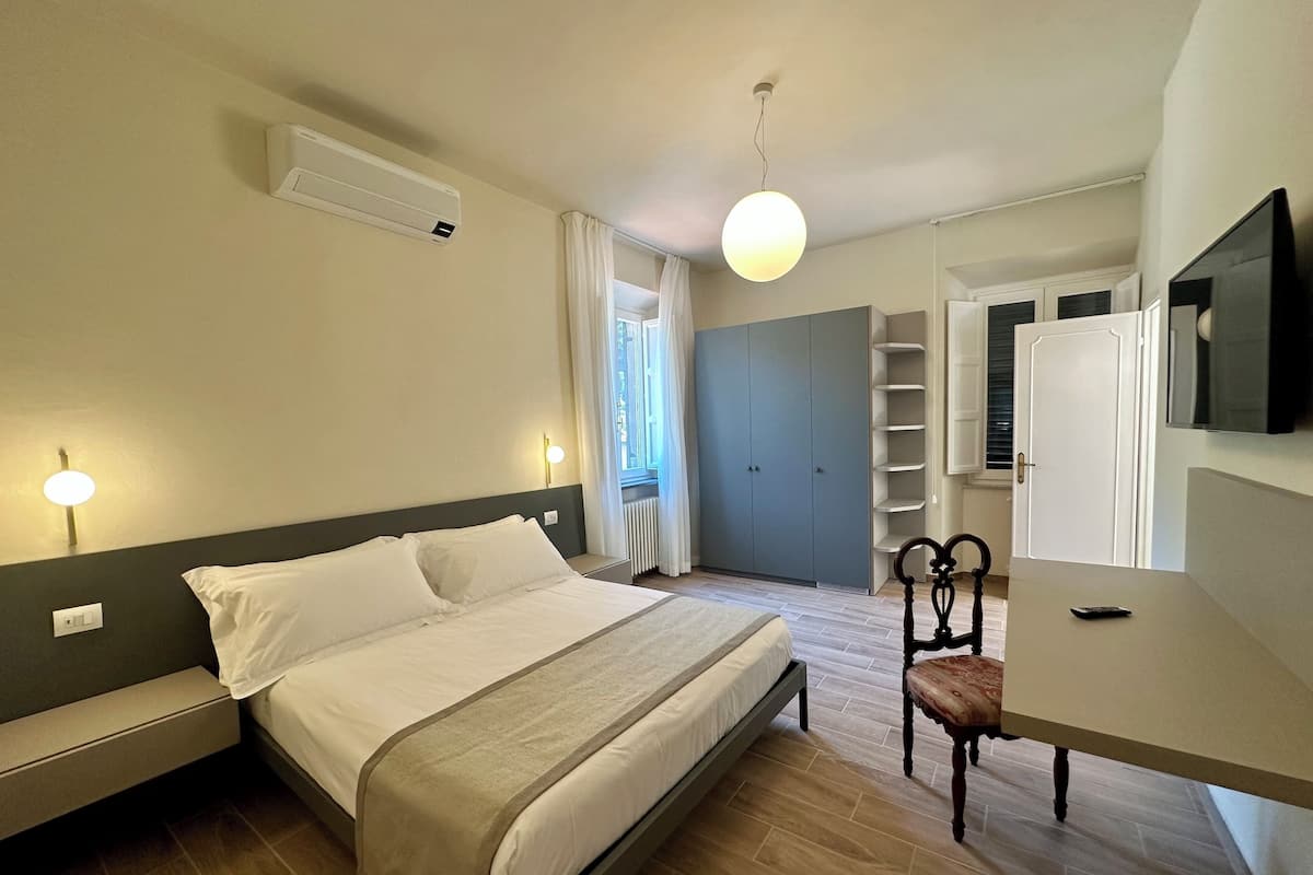 A bedroom with a bed, bedside tables, a chair, a desk, a TV, and a wardrobe.