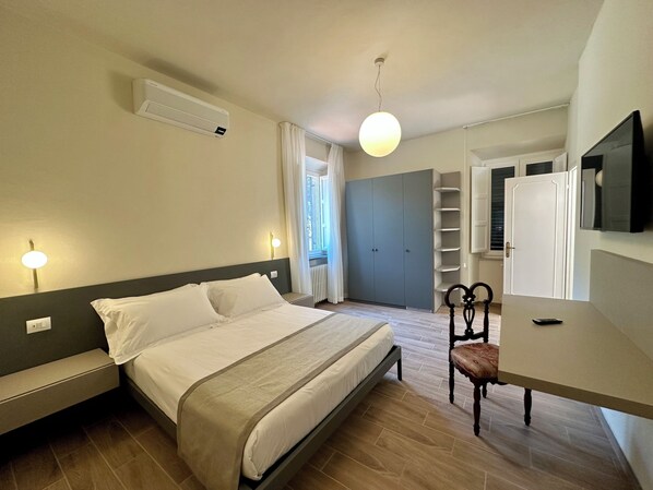 A bedroom with a bed, bedside tables, a chair, a desk, a TV, and a wardrobe. - La Ninfa Hotel (Bagni di Lucca)