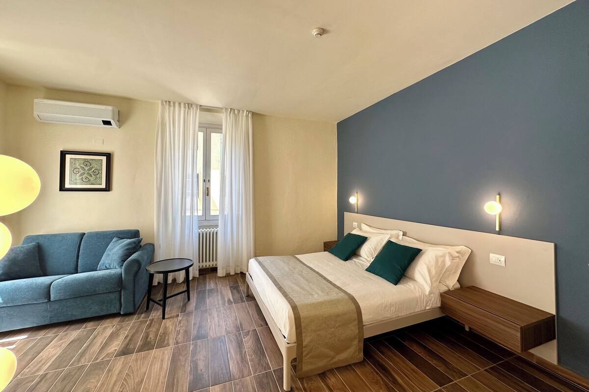 A hotel room with a bed, bedside table, nightstand, and a small seating area with a sofa and a table.