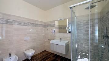 A modern bathroom with a glass shower enclosure, a toilet, a bidet, and a vanity with a mirror.