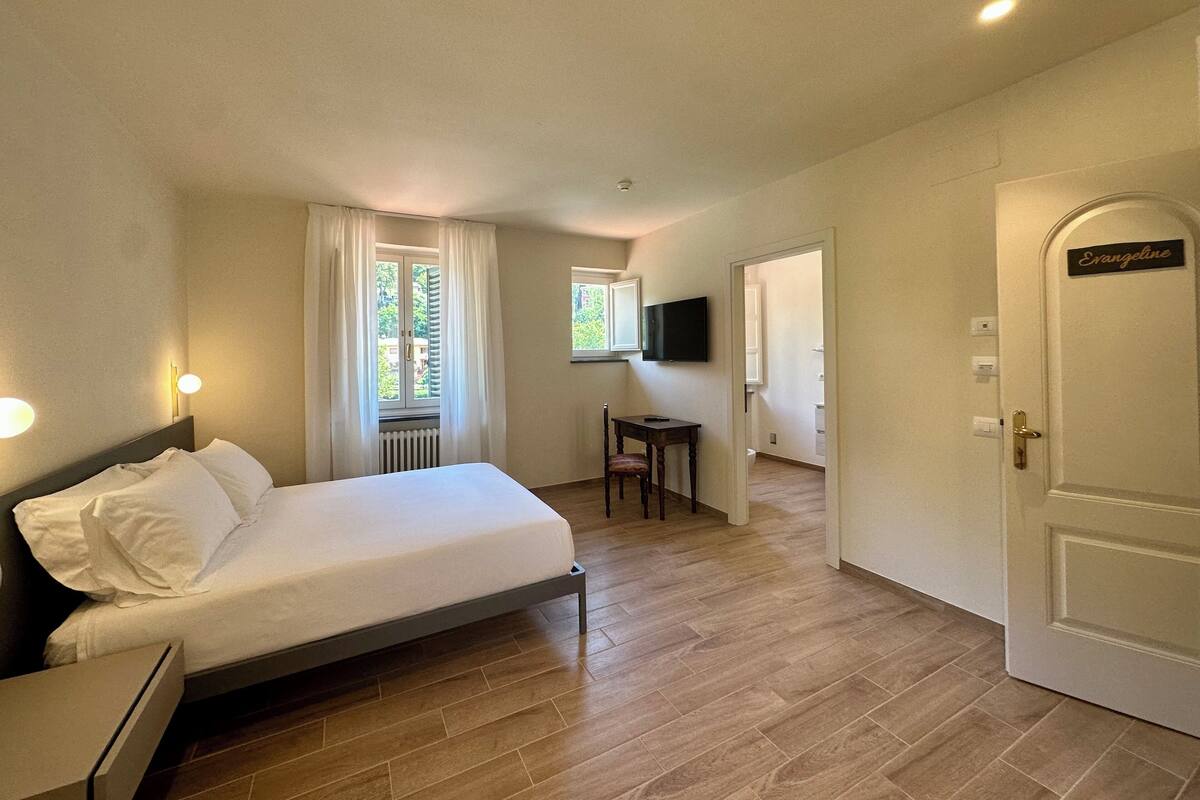 A bedroom with a bed, a desk, a chair, a television, and a door labeled "Evangeline".