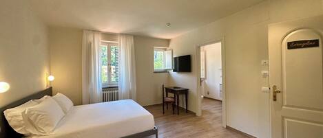A bedroom with a bed, a desk, a chair, a television, and a door labeled "Evangeline".