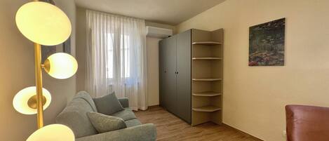 A modern living room with a grey sofa, a floor lamp, a wardrobe, and a painting on the wall.
