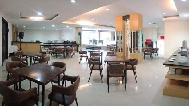 A spacious dining area with multiple tables and chairs, a central column, and a kitchen area in the background. - ALL NITE & DAY Makassar (Makassar)
