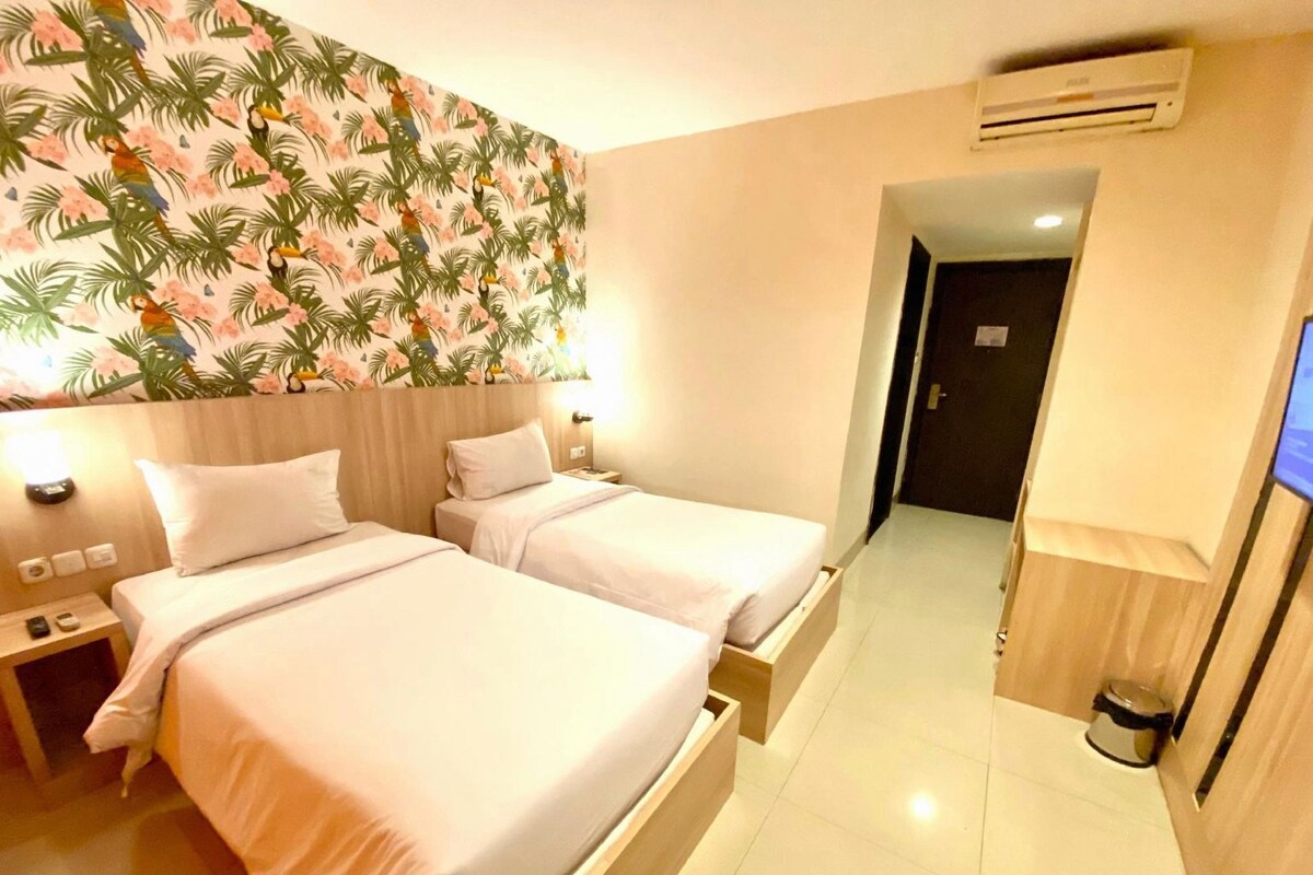 Una habitación de hotel con dos camas, aire acondicionado en la pared y un televisor también en la pared.