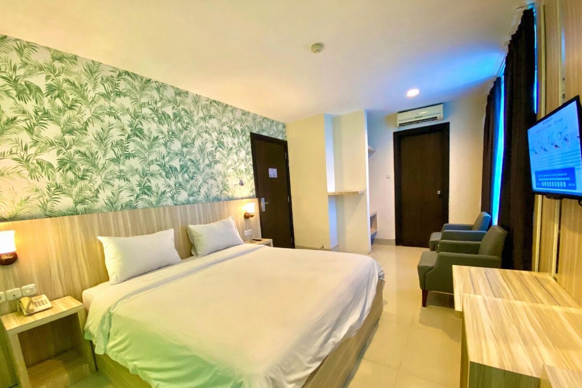A hotel room with a large bed, a desk, a television, and a wall with a tropical leaf pattern.