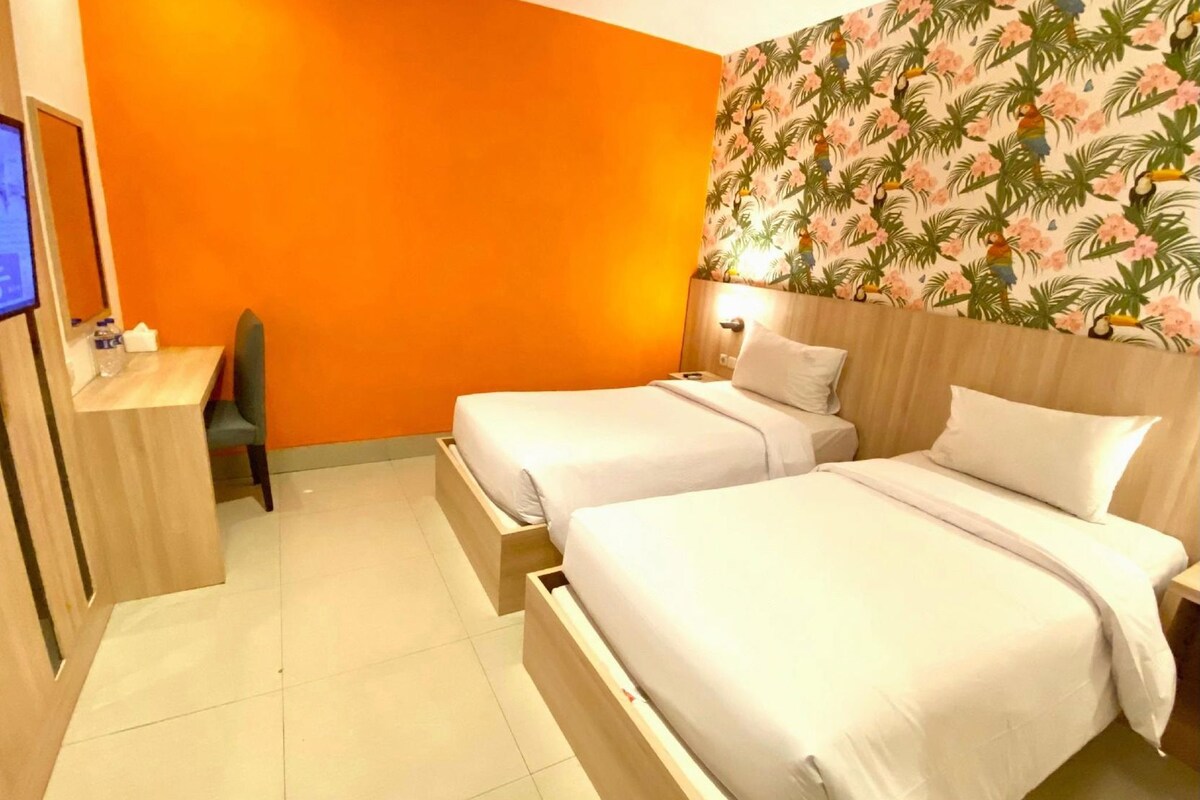 A hotel room with two beds, a desk, and a television.