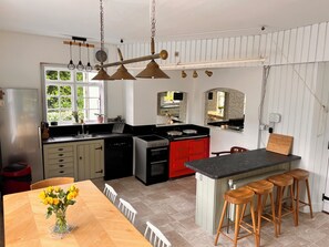 Una cocina con una isla central, una mesa de comedor con sillas y vistas al exterior a través de una ventana.