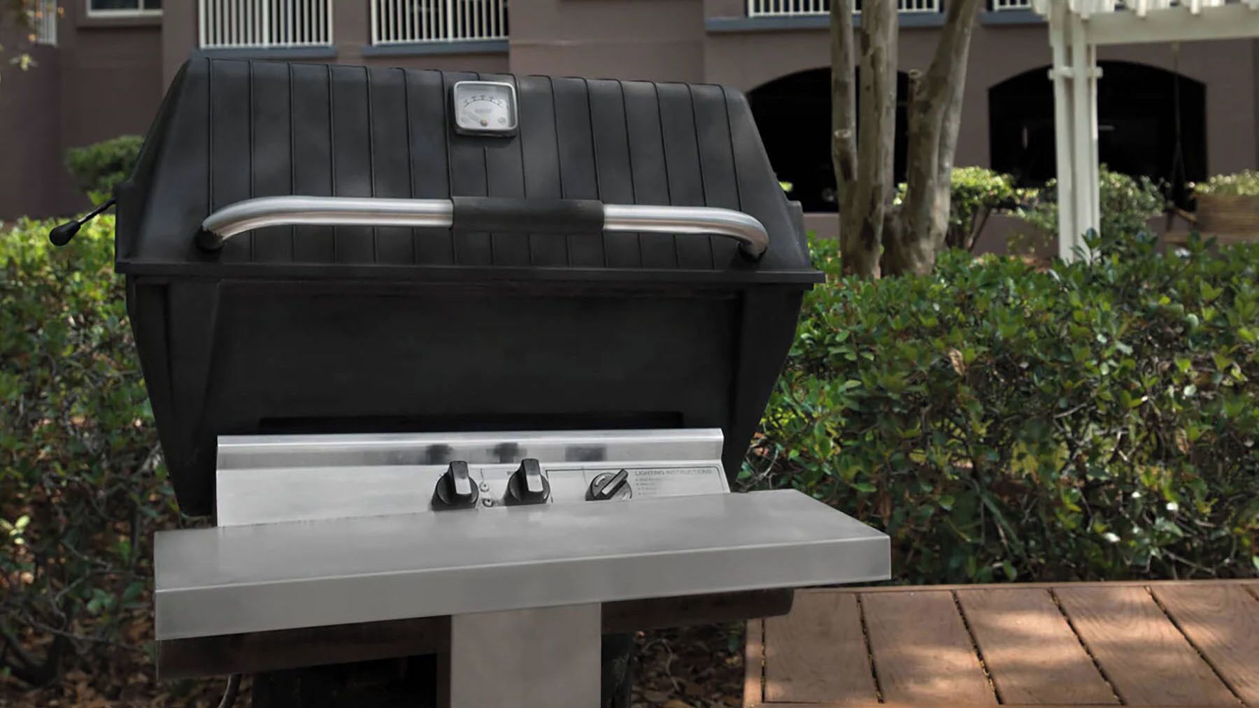 Ein Grill mit digitalem Thermometer und Bedienelementen steht auf einer Terrasse mit einem Holztisch davor.