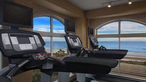 Et fitnesscenter med løbebånd og store vinduer med udsigt over havet.