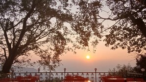 An outdoor seating area with tables and chairs, overlooking a sunset. - The Byke Laxmi Resort (Karjat)