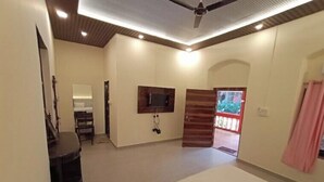 A bedroom with a bed, a TV mounted on the wall, a ceiling fan, and a door leading to an outdoor area. - The Byke Laxmi Resort (Karjat)