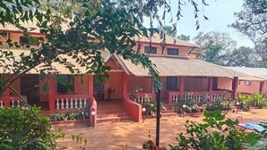 A two-story building with a red facade, a tiled roof, and a covered outdoor area with plants and seating. - The Byke Laxmi Resort (Karjat)