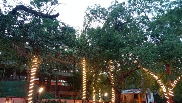 A courtyard with trees, string lights, and a small building. - The Byke Laxmi Resort (Karjat)