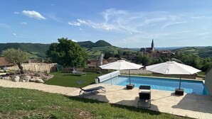 Ein Pool mit Liegestühlen und Sonnenschirmen, umgeben von einer Rasenfläche und einer Steinmauer.