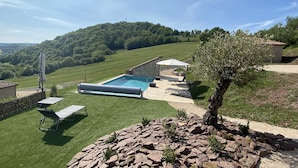 Ein Schwimmbad mit einer Terrassenanlage, einer Steinmauer und Blick auf eine hügelige Landschaft.