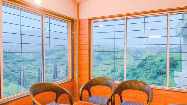 A room with a table and four chairs, large windows with a view of a bridge and greenery, and a ceiling fan. - Oxi Valley Resort (Igatpuri)