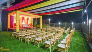 An outdoor event space with rows of chairs and a stage, surrounded by a fence and illuminated by overhead lights. - Oxi Valley Resort (Igatpuri)