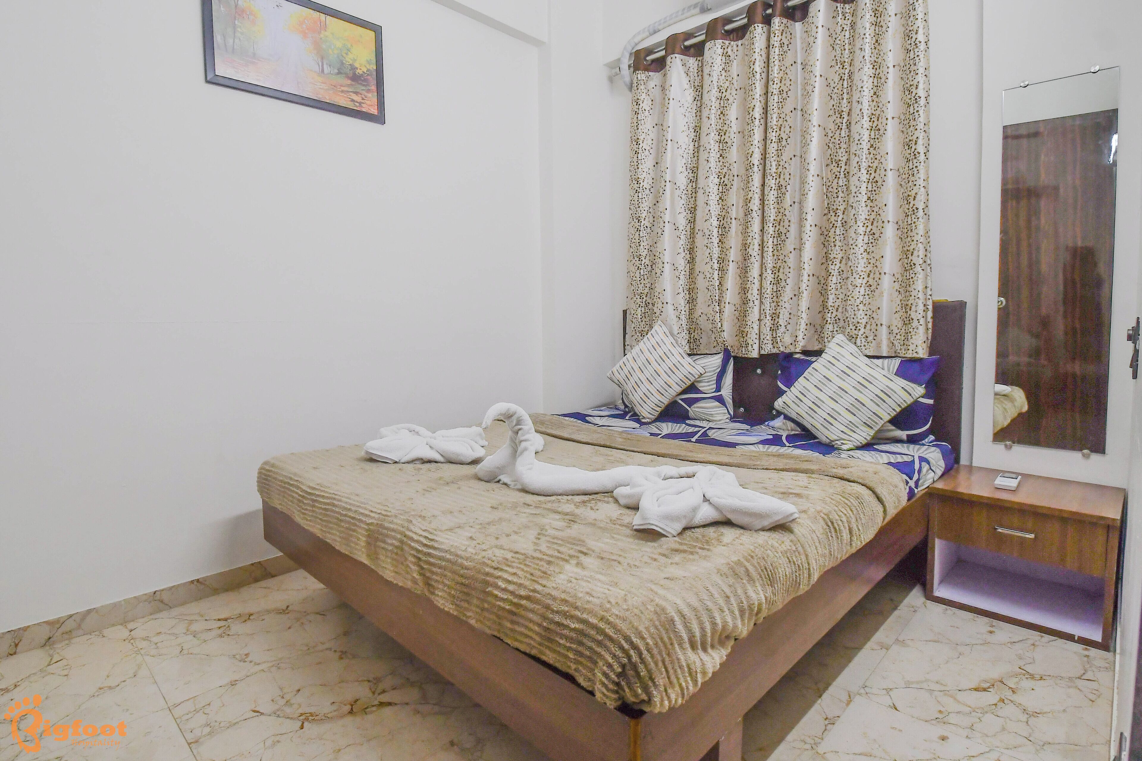 Un dormitorio con cama, mesita de noche, espejo y un cuadro en la pared.