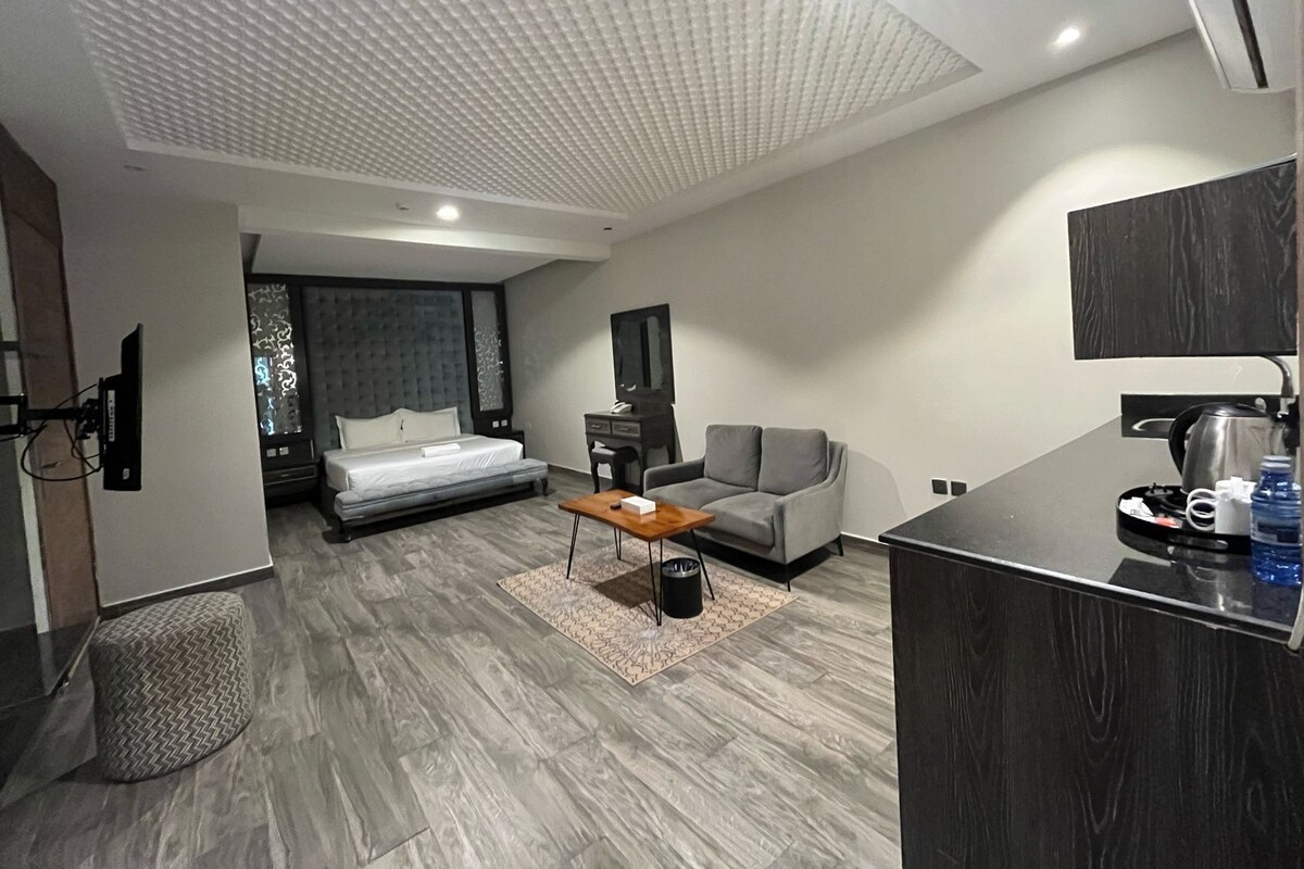 Et moderne hotelværelse med seng, sofa, sofabord og et tekøkken.
