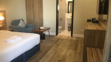 A hotel room with a bed, a sofa, a small table, a desk, a mirror, a shower, and a bathroom.