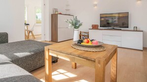 Ett modernt vardagsrum med ett träbord, en soffa, en tv och ett köksområde med skåp och ett kylskåp.