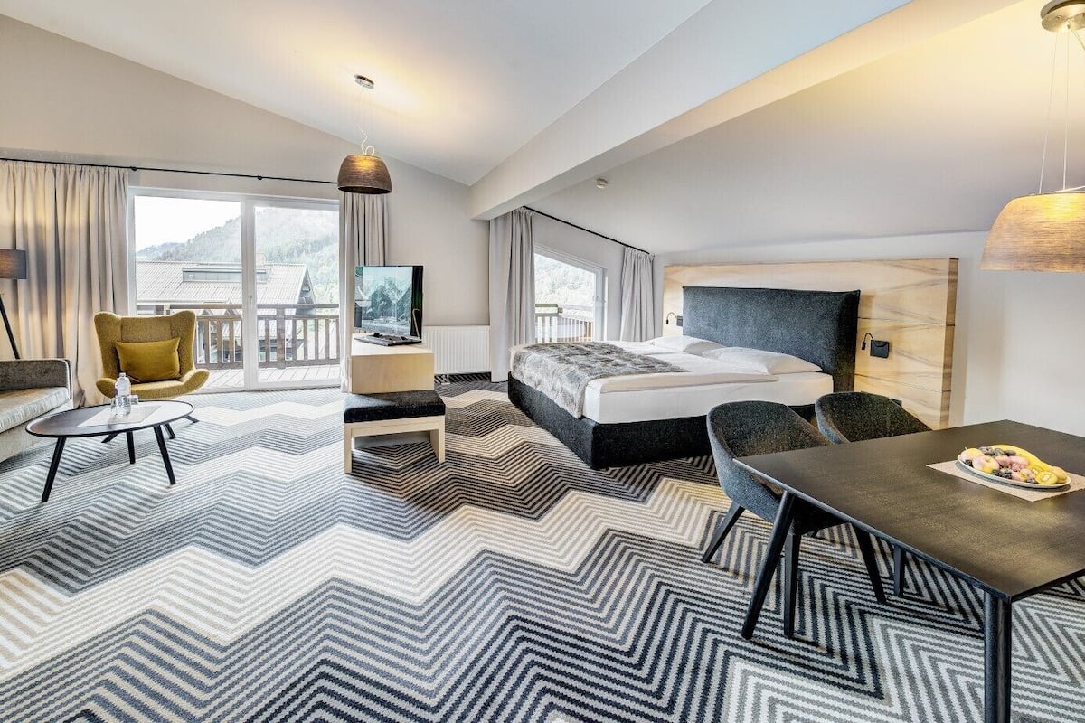 A modern hotel room with a large bed, a sofa, a dining table, and a TV.
