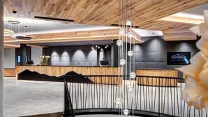 Un'area reception moderna con soffitto in legno, una scrivania reception e un grande schermo che mostra il nome dell'hotel.