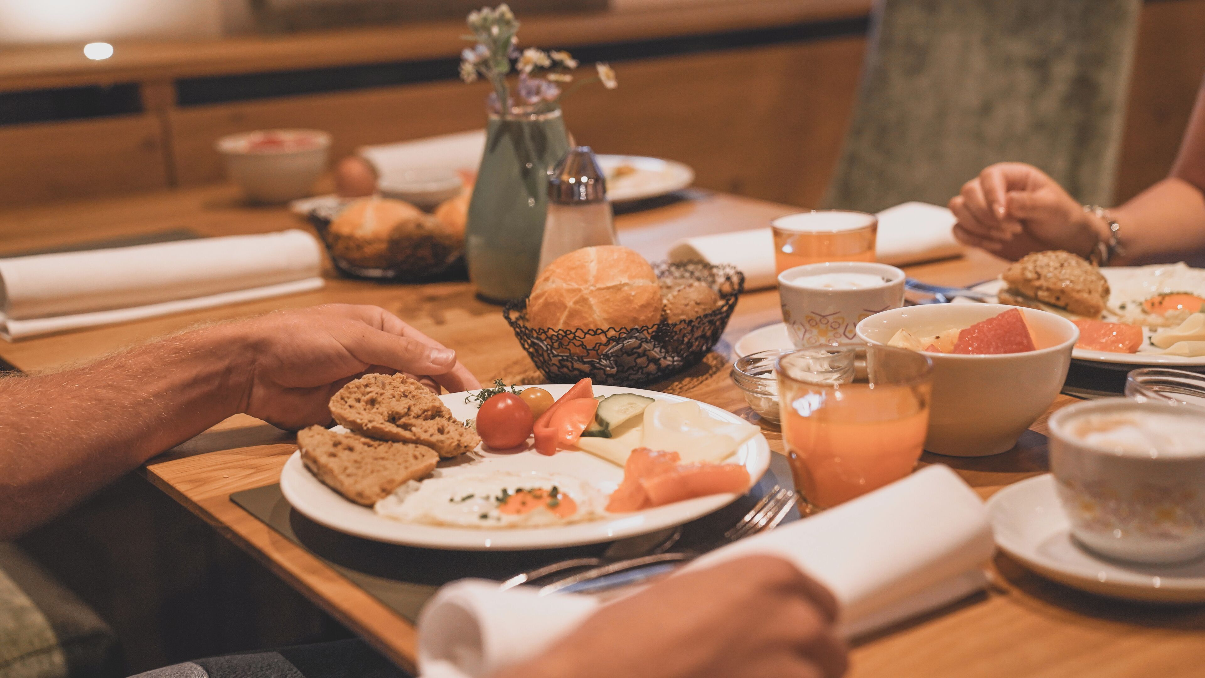 Una mesa de comedor con diferentes alimentos y una persona alcanzando una rebanada de pan.