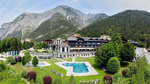 Un hotel con piscina, immerso nel verde e circondato da montagne.
