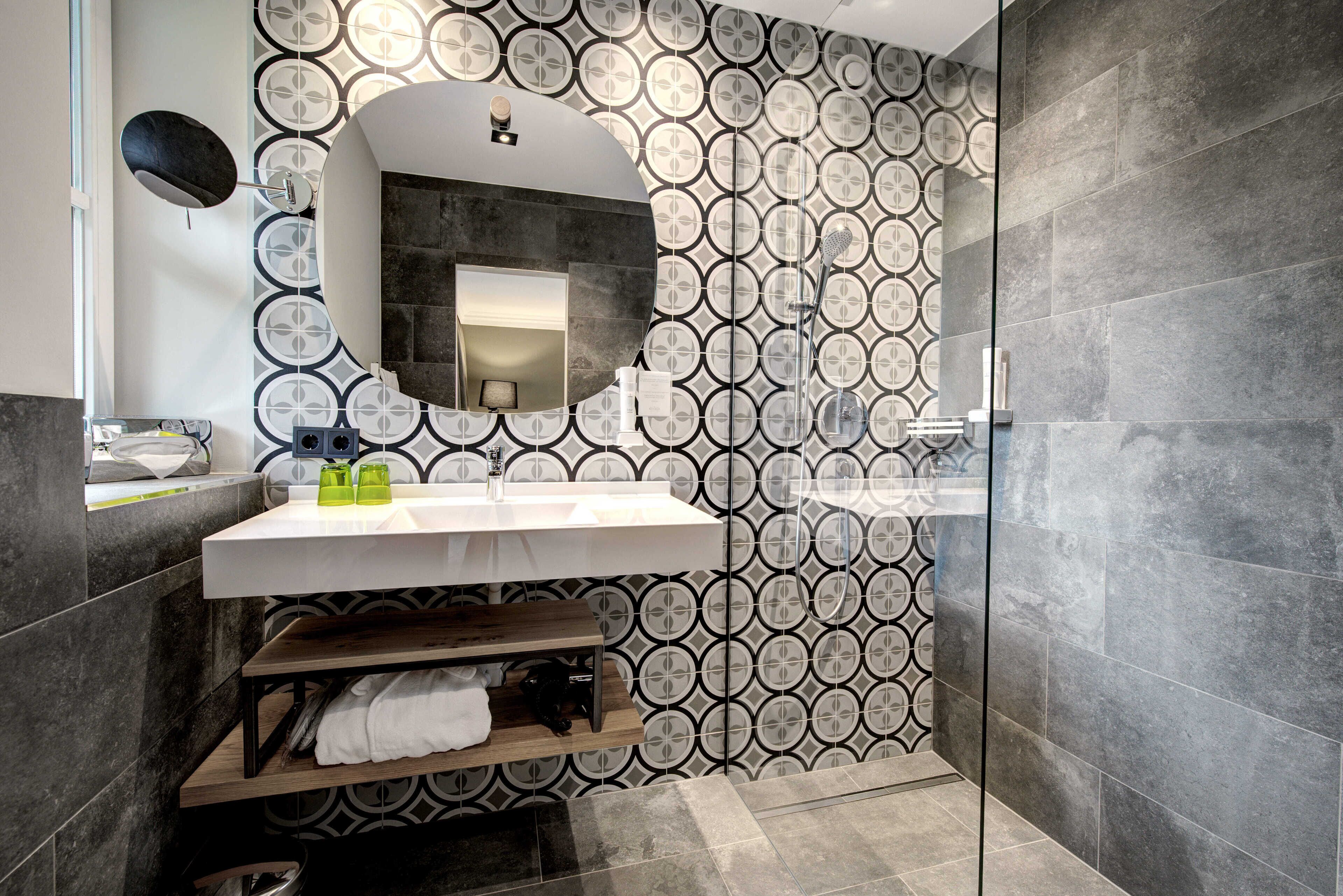 Un baño moderno con un espejo grande, lavamanos blanco y azulejos con diseño.