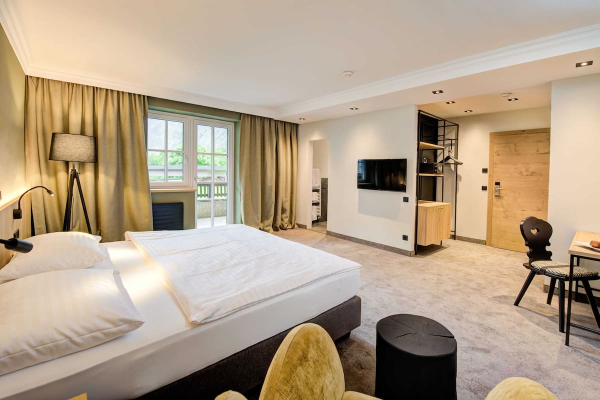 A hotel room with a large bed, a desk, a chair, a TV, and a wardrobe.