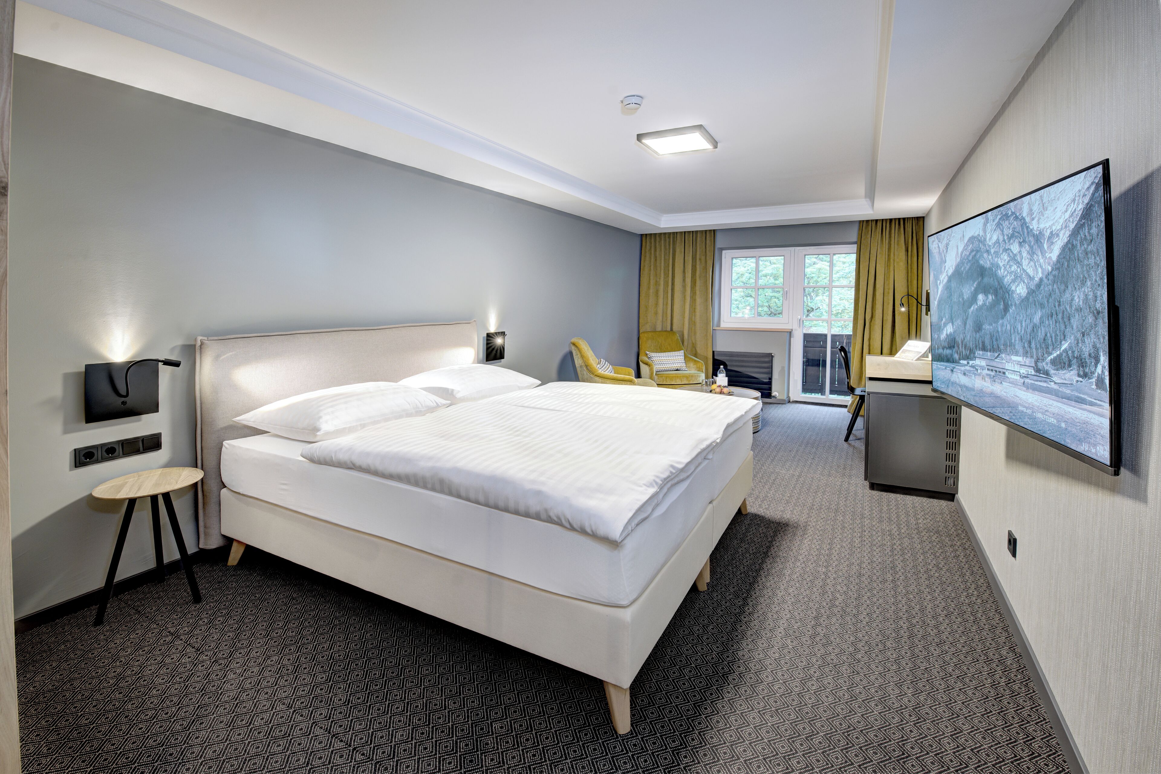 Quarto de hotel com uma cama grande, uma escrivaninha, uma cadeira, uma televisão e vista para o exterior.
