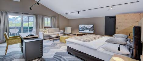 Quarto moderno com cama grande, escrivaninha, cadeira, televisão e vista para montanhas pela janela.