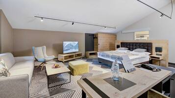 A modern hotel room with a sofa, armchair, wooden bed, and a TV.