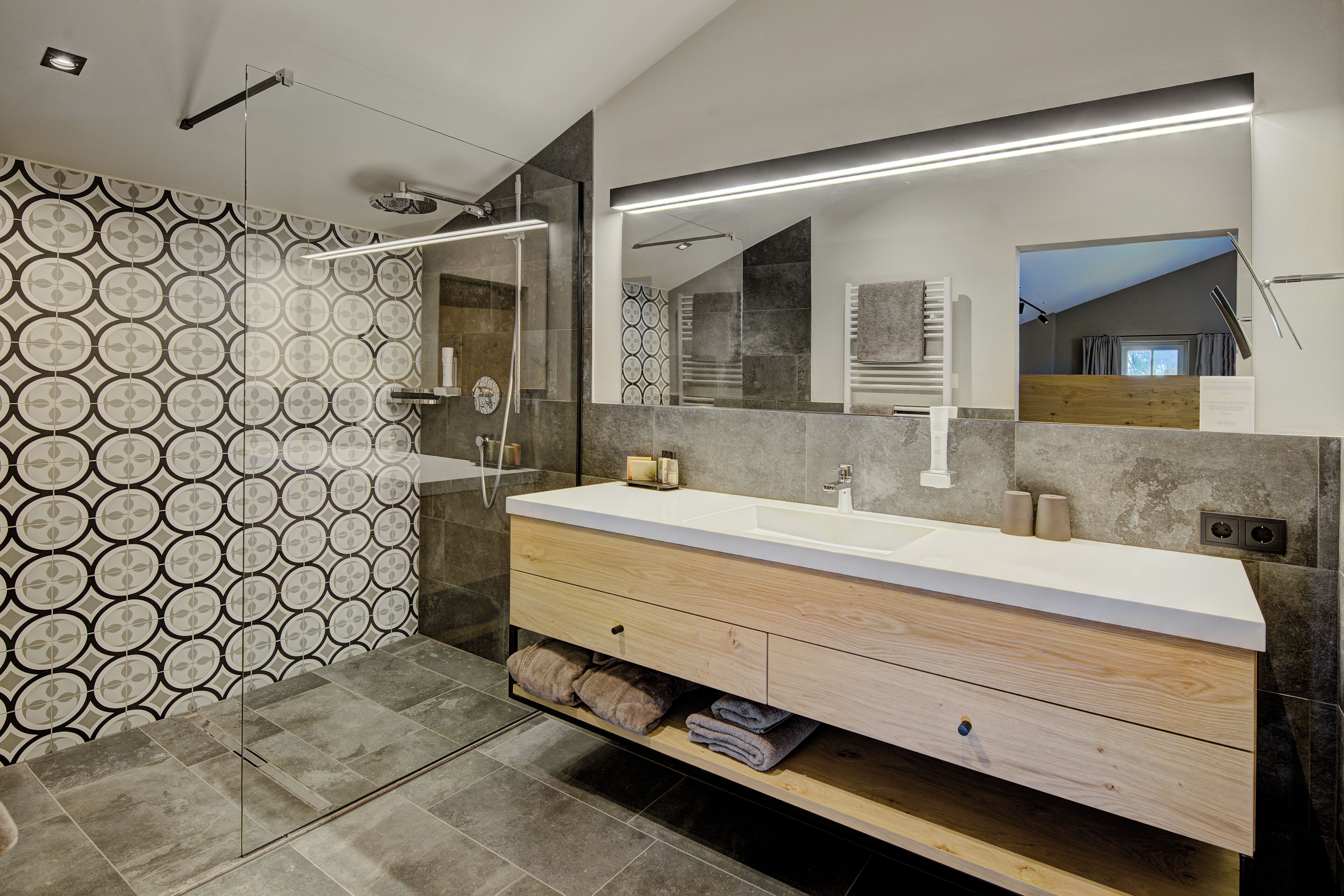 A modern bathroom with a large mirror, a wooden vanity, and a patterned wall.