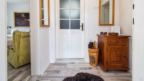 Een hal met een witte deur, een spiegel, een houten kast en een groene fauteuil.