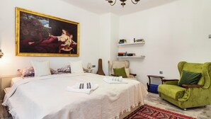 Een slaapkamer met een groot bed, een groene fauteuil, een boekenkast en een kroonluchter.