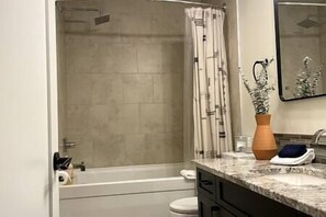 Un baño con ducha, inodoro y encimera de mármol con un jarrón y una toalla.