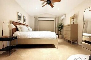 Un dormitorio con cama, mesita de noche, cómoda, ventilador de techo y ventana con cortinas.
