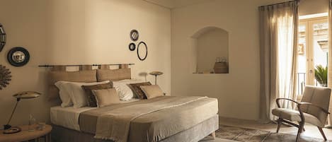 Un dormitorio con una cama grande, mesitas de noche, una silla y una ventana con cortinas.