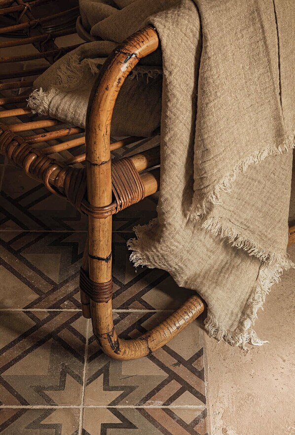 A wicker chair with a wooden frame and a frayed fabric cover. - Dimora Santagatha (Noto)