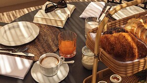 A breakfast setup with a wicker table, plates, cups, a basket of bread, and a potted plant. - Dimora Santagatha  (Noto)
