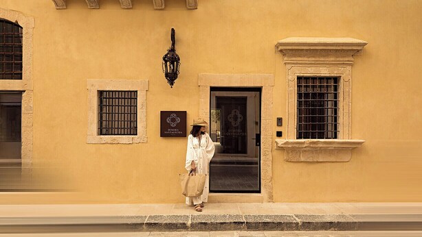 A woman walking past a building with a sign reading "DIMORA SANTAGATHIA". - Dimora Santagatha  (Noto)
