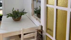 Un rincón de una habitación con una mesa blanca, un espejo con marco decorativo y una puerta con un panel de vidrio dorado.