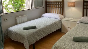 Un dormitorio con dos camas individuales, una ventana con vista a árboles, un radiador y una mesita de noche con una lámpara.