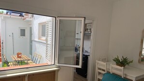 Un espacio habitable compacto con un ventanal corredera que da a un balcón, un sofá color turquesa, una mesita y una planta en maceta.