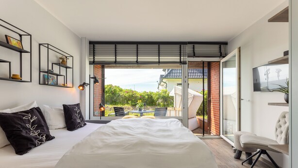 A modern bedroom with a large bed, a TV, and a sliding glass door leading to a balcony. - Isola - Wenningstedt-Braderup (Sylt) (Wenningstedt-Braderup (Sylt))