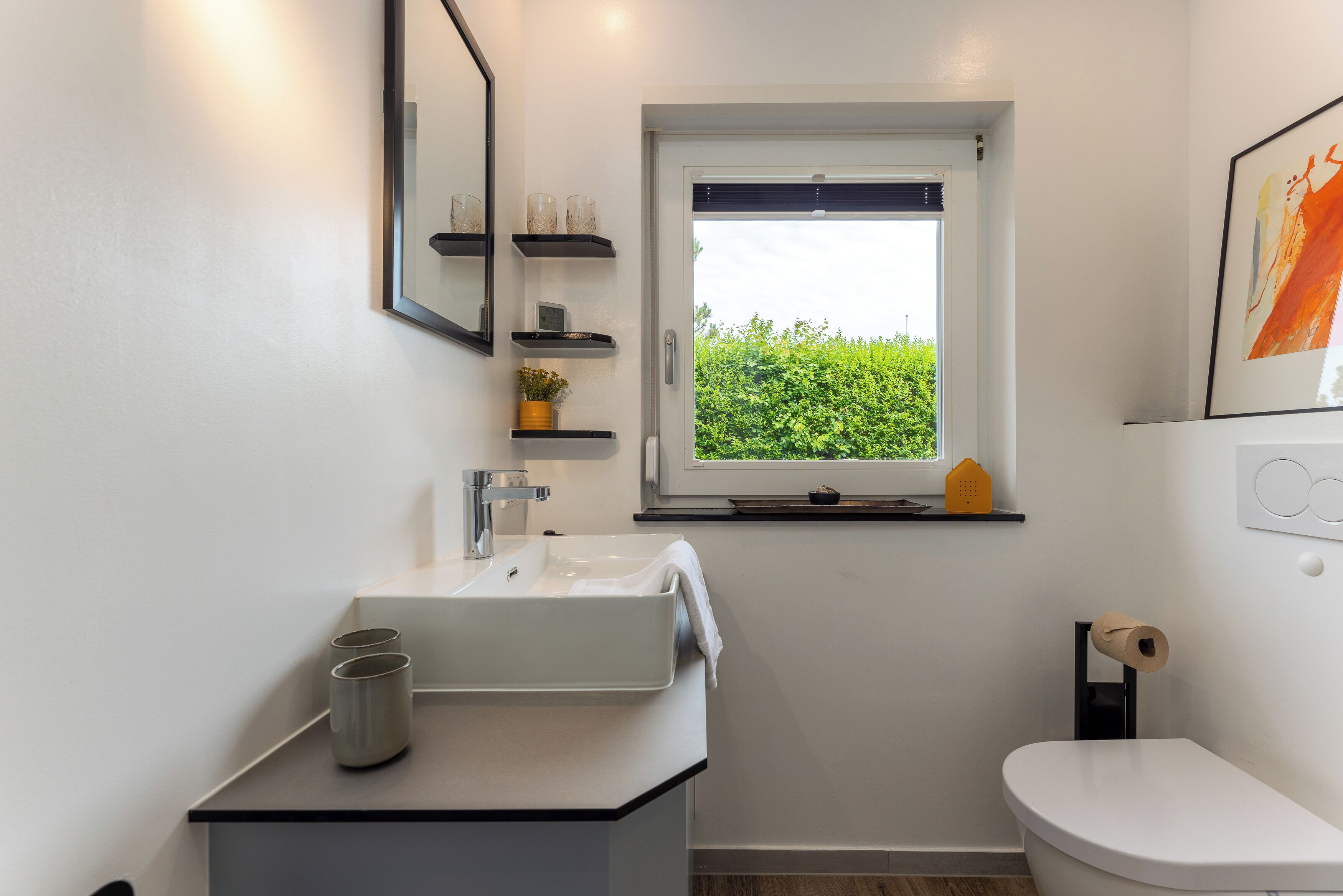 Et moderne badeværelse med en hvid vask, toilet og et vindue med udsigt til grøn natur.