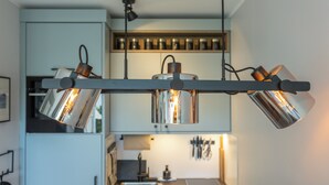 A kitchen with modern pendant lights, a wooden shelf with jars, and a visible refrigerator. - Isola - Wenningstedt-Braderup (Sylt) (Wenningstedt-Braderup (Sylt))
